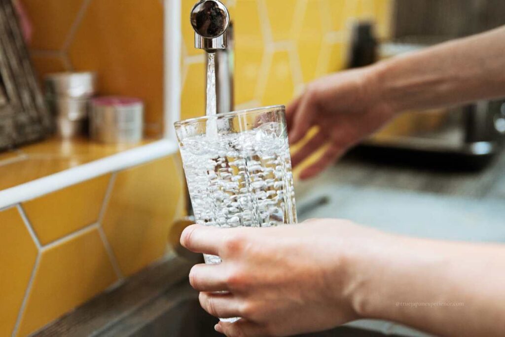 Filling a glass with clean tap water from a kitchen faucet.