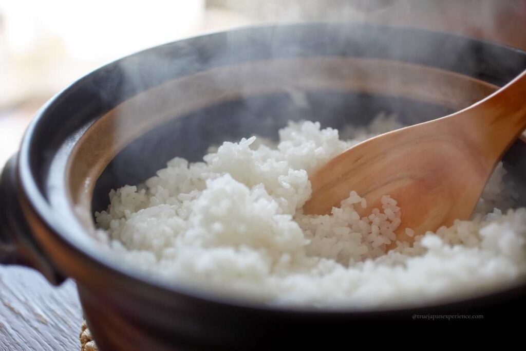 Steaming Japanese white rice cooked in a donabe clay pot, stirred with a wooden rice paddle.