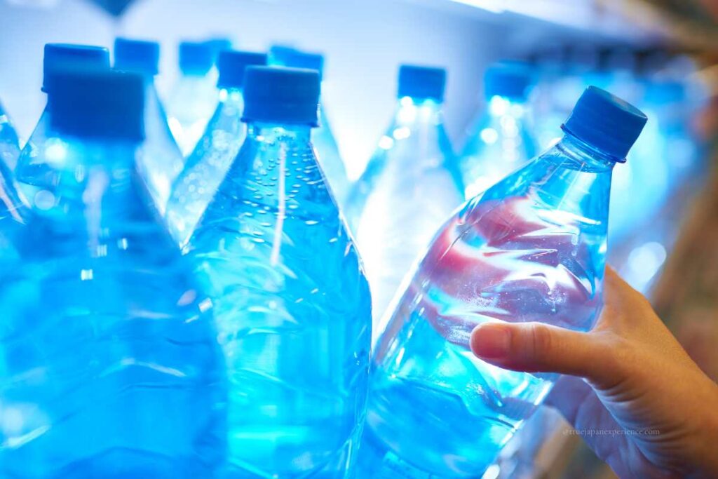 A hand picking up a bottle of mineral water from a refrigerated shelf in a store.