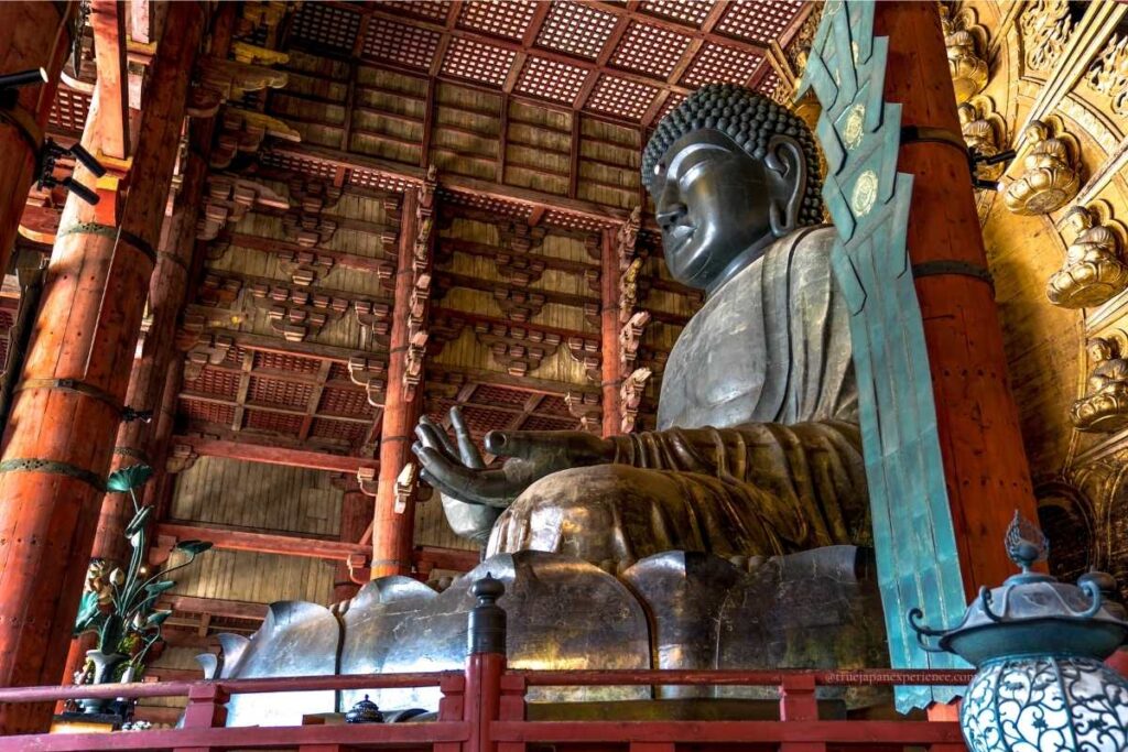 Angled side view of the Great Buddha statue at Todai-ji Temple in Nara, Japan, showing wooden pillars and temple interior details