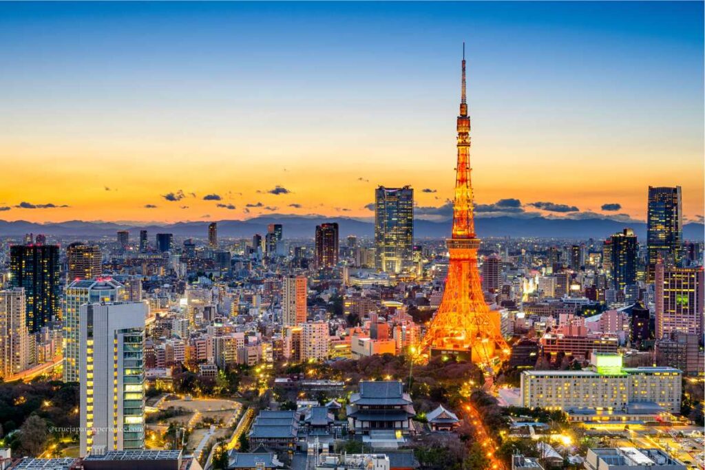 Tokyo Tower illuminated at dusk, surrounded by city lights and a glowing orange sky.