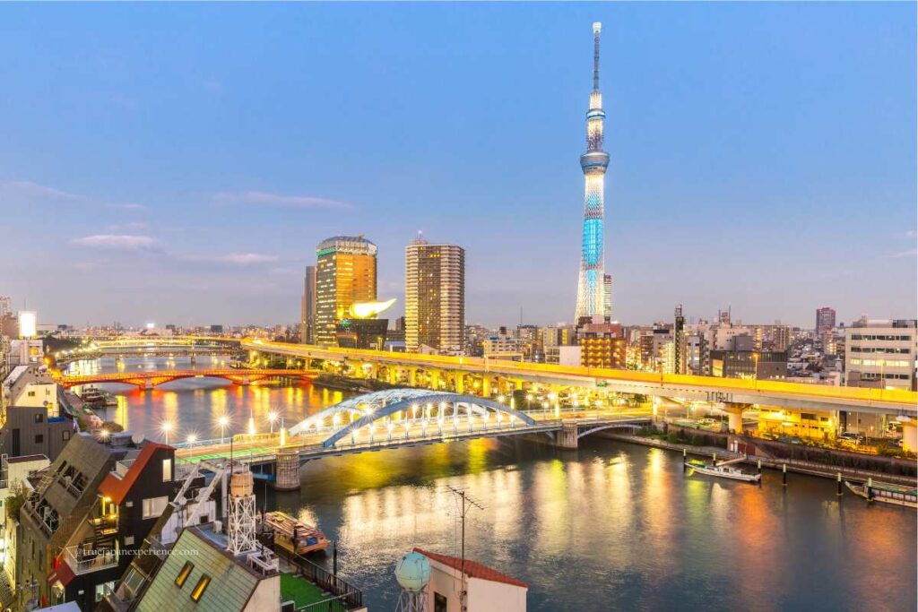 Tokyo Skytree illuminated in blue at twilight, overlooking the Sumida River and colorful bridges in Asakusa.