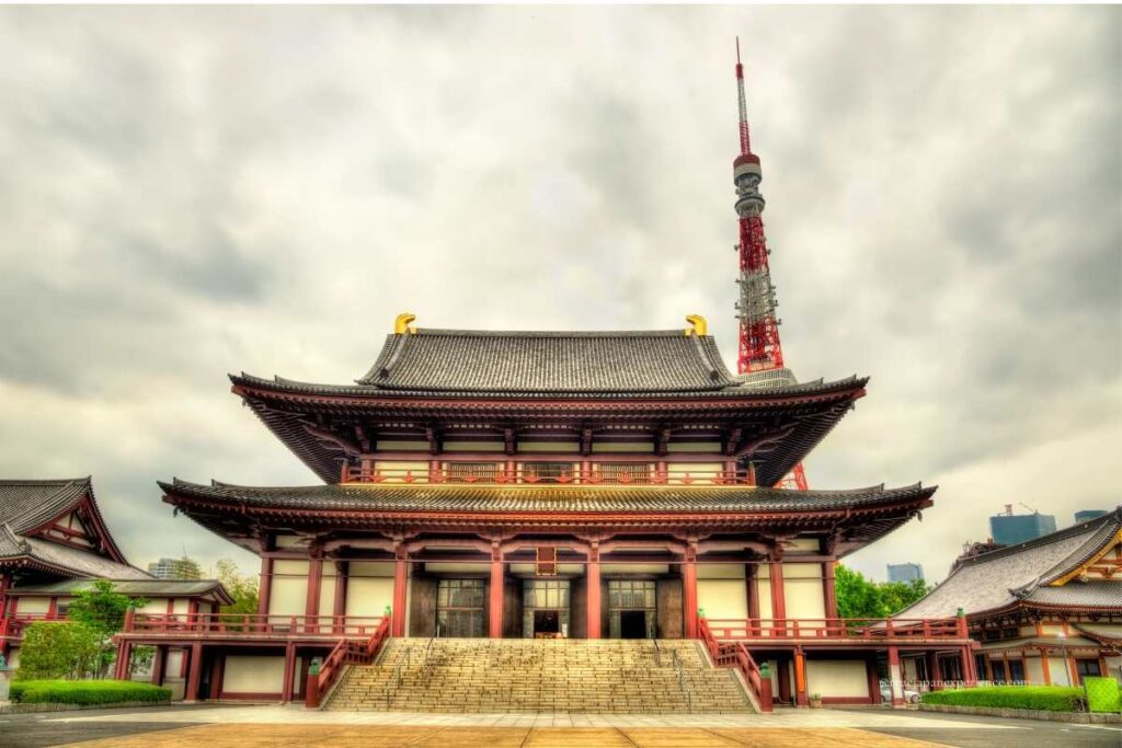Zojoji Temple with its traditional wooden architecture, framed by the towering Tokyo Tower in the background under a cloudy sky.