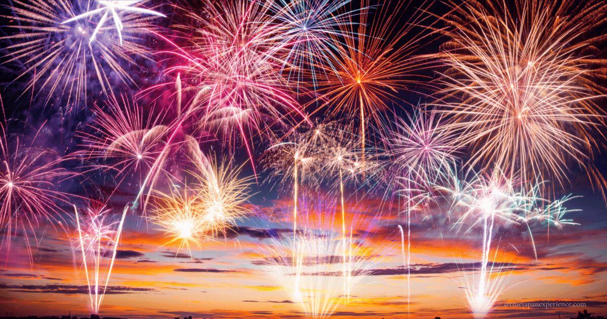Colorful fireworks exploding in the evening sky during sunset in Japan, with orange and purple tones lighting up the background.