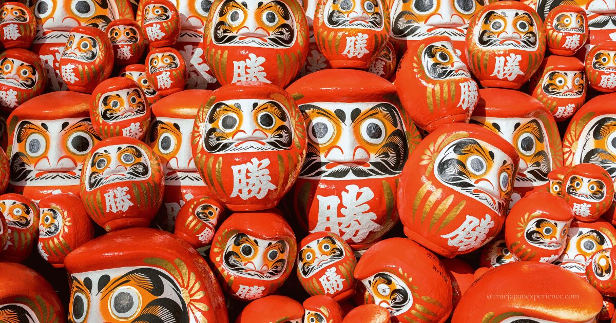 A colorful display of many red Daruma dolls with bold white kanji for “victory,” symbolizing luck and perseverance in Japan.