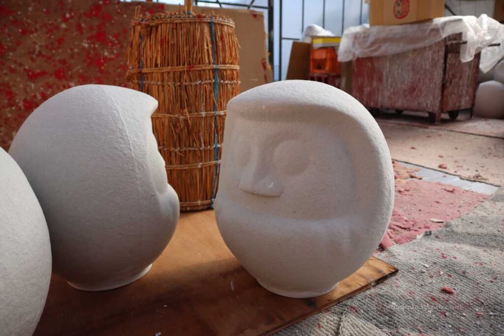 Unpainted paper-mache Daruma dolls drying in a workshop before being decorated with colors.