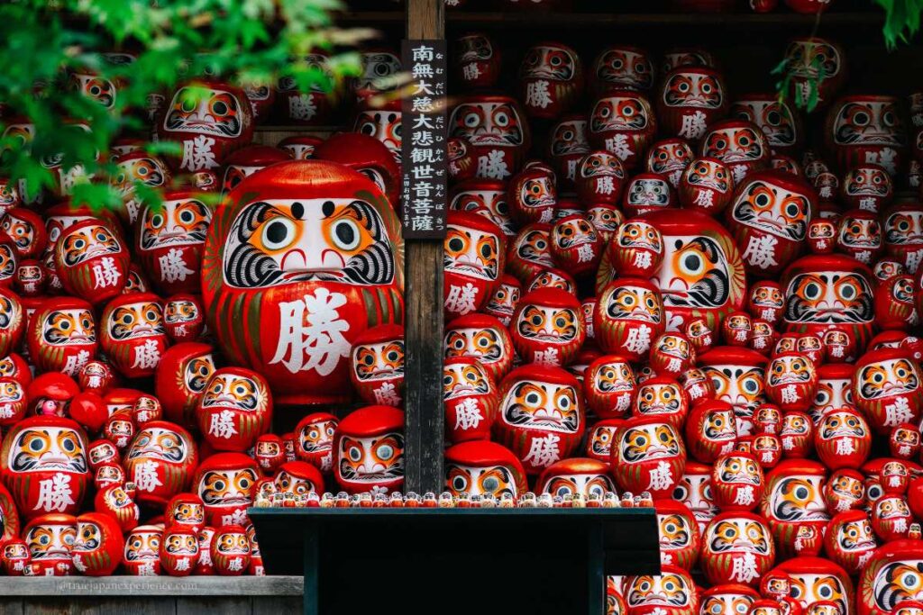 Hundreds of red Daruma dolls with bold eyes and the kanji for “victory” stacked at a Japanese temple altar.