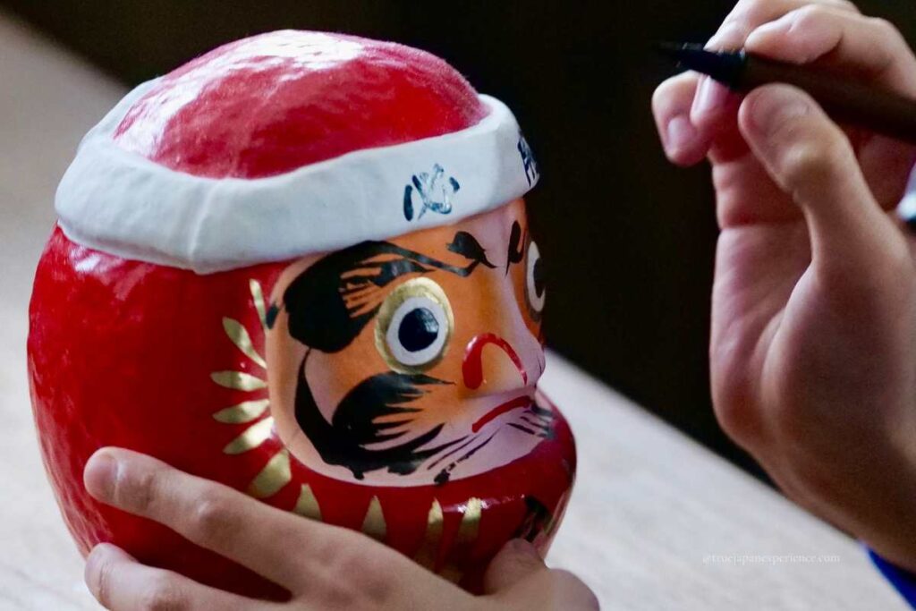 Person drawing the eye of a red Daruma doll with a brush, a tradition when making a wish.