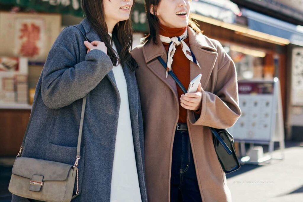 Two women smiling and walking outdoors with handbags, enjoying sightseeing in Japan.
