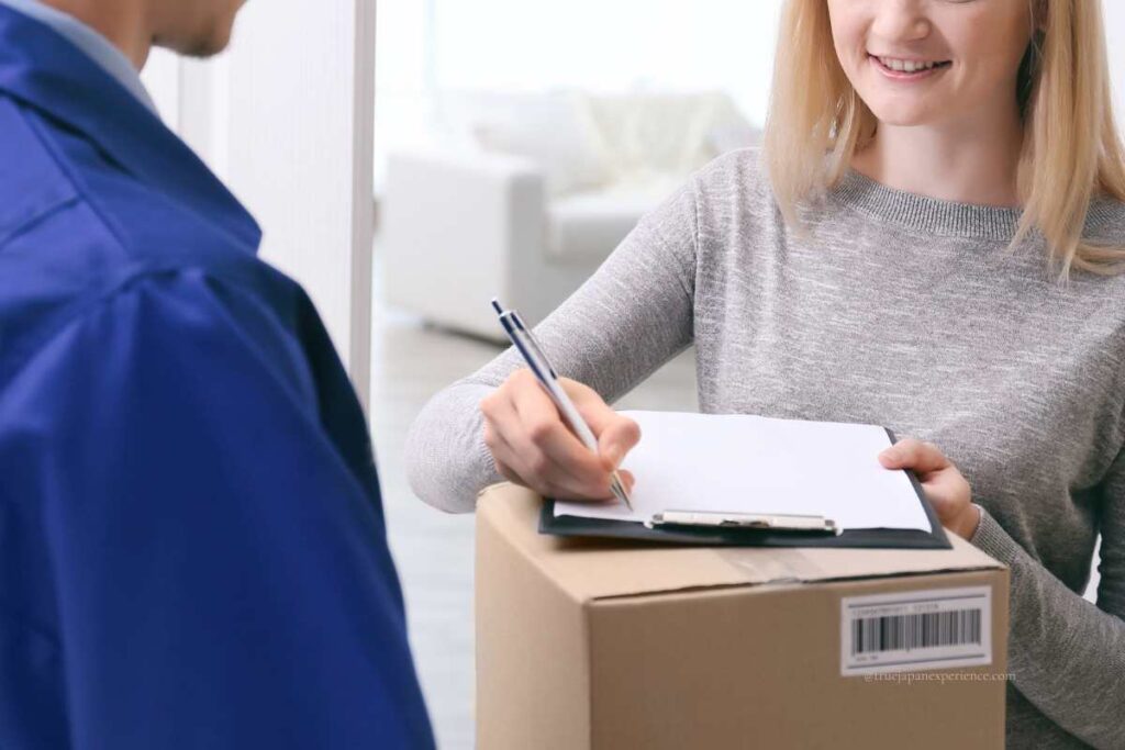 A woman signing a delivery form while receiving a cardboard package from a courier at her door.