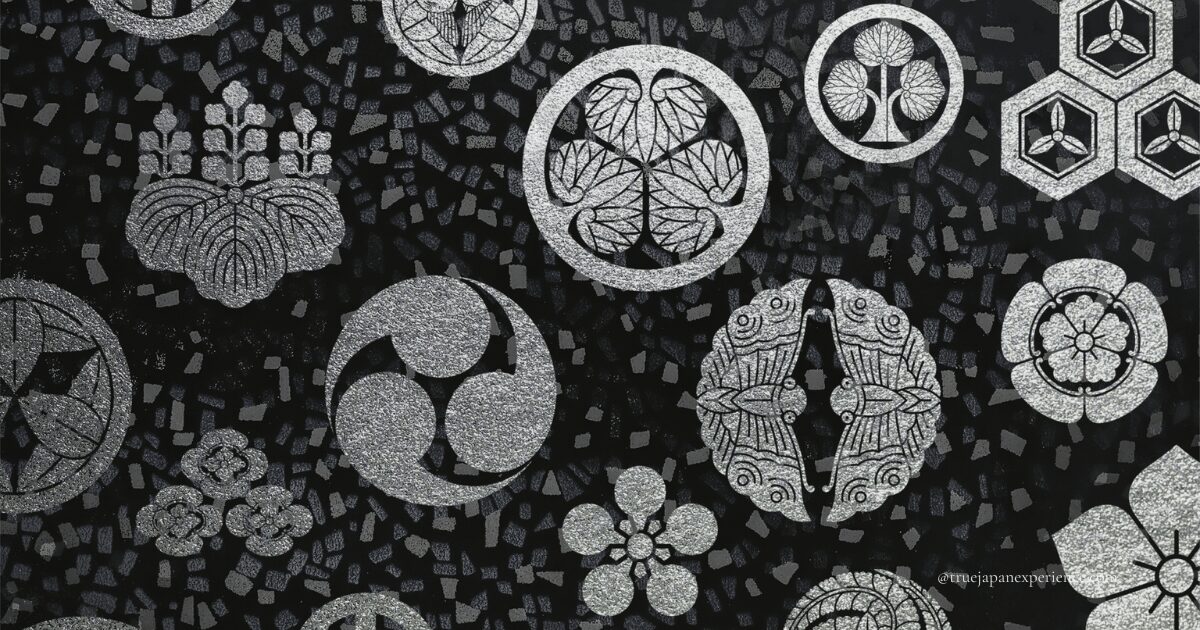 Various traditional Japanese family crests (kamon) in silver on a black patterned background, including paulownia, hollyhock, and butterfly motifs.