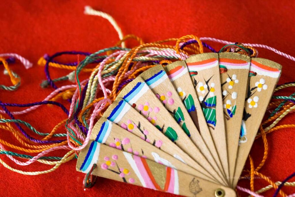 Wooden Japanese folding fan (sensu) with hand-painted floral designs and colorful decorative cords on red background
