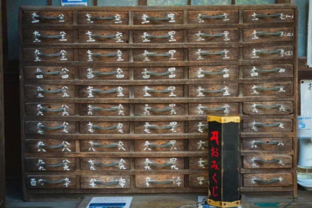 Traditional omikuji fortune drawers and a black omikuji box with red lettering at a Japanese shrine or temple.