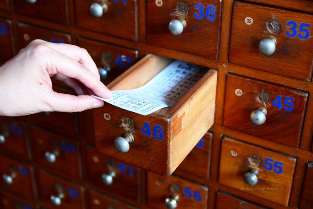 A person pulling out an omikuji paper from drawer number 46 at a Japanese shrine.