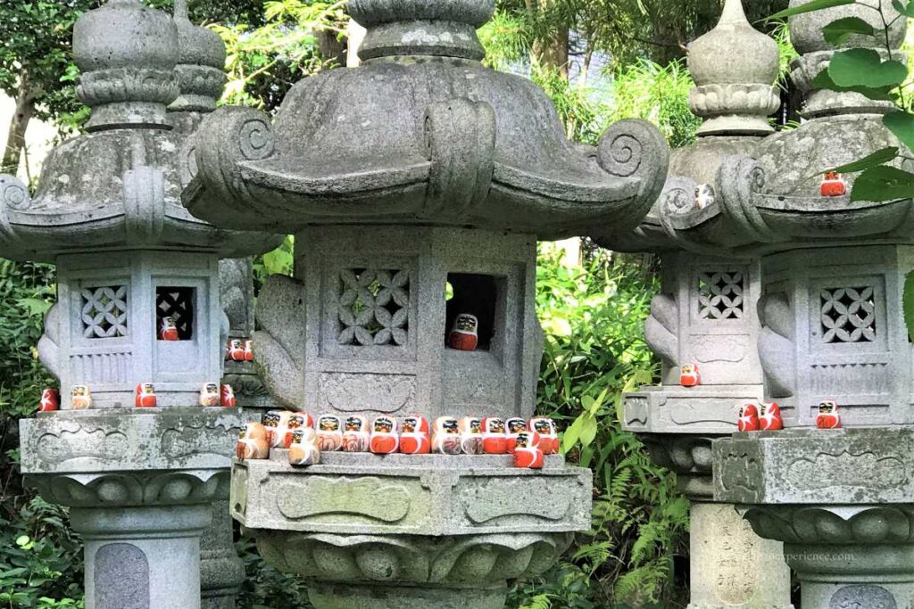 Small daruma dolls placed on and inside stone lanterns at Katsuoji Temple, creating a charming scene among the greenery.