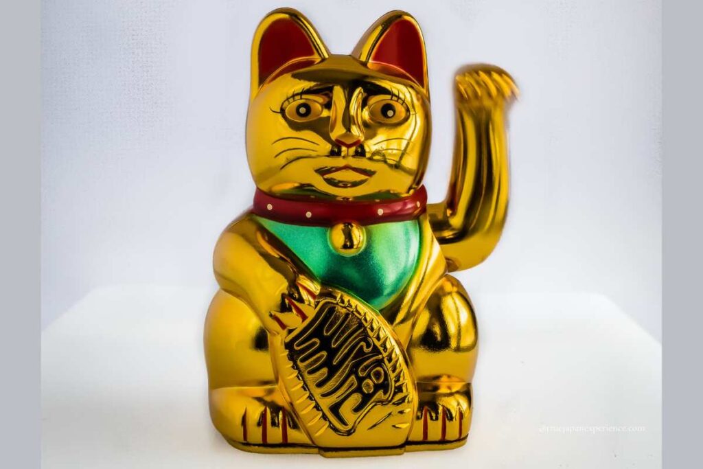 Golden Maneki-neko statue with a raised paw, holding a koban coin, symbolizing wealth and good fortune.