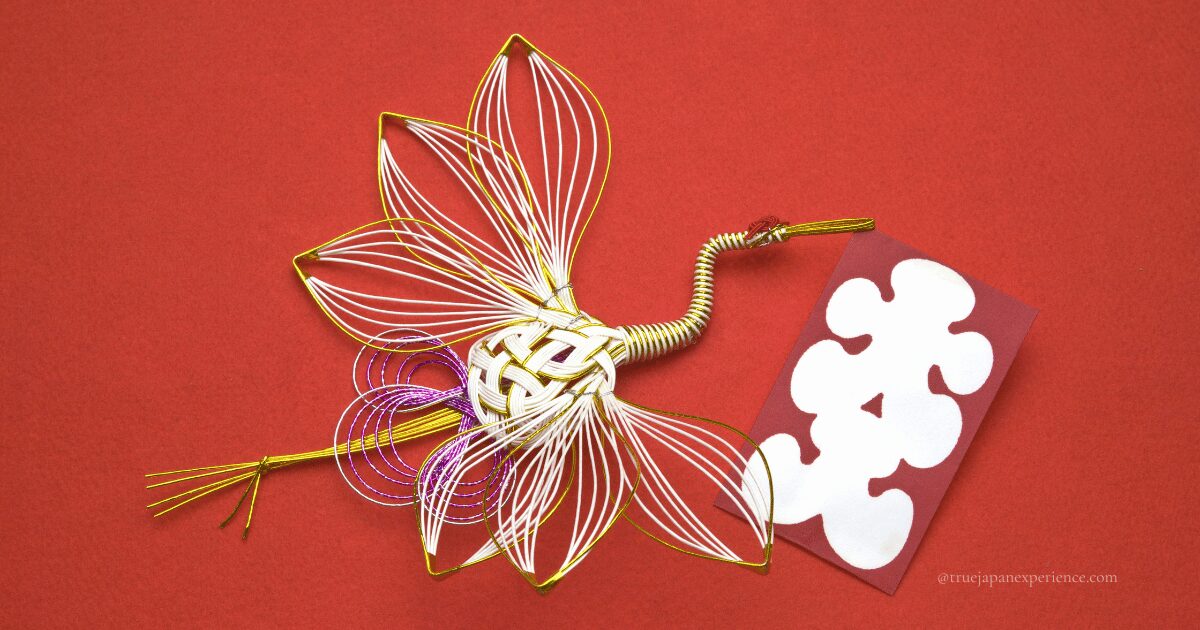 This is a mizuhiki craft made of gold and white paper string woven into the shape of a crane on a red background.