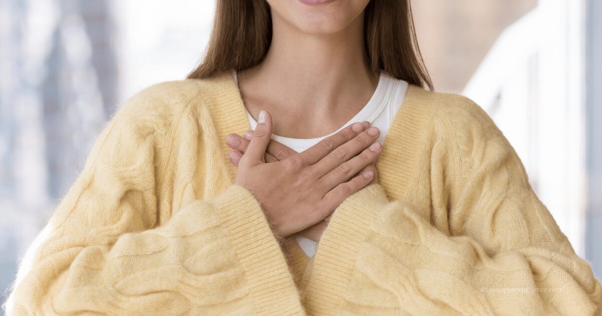 A woman smiling gently with both hands placed over her heart, expressing warmth and sincerity.