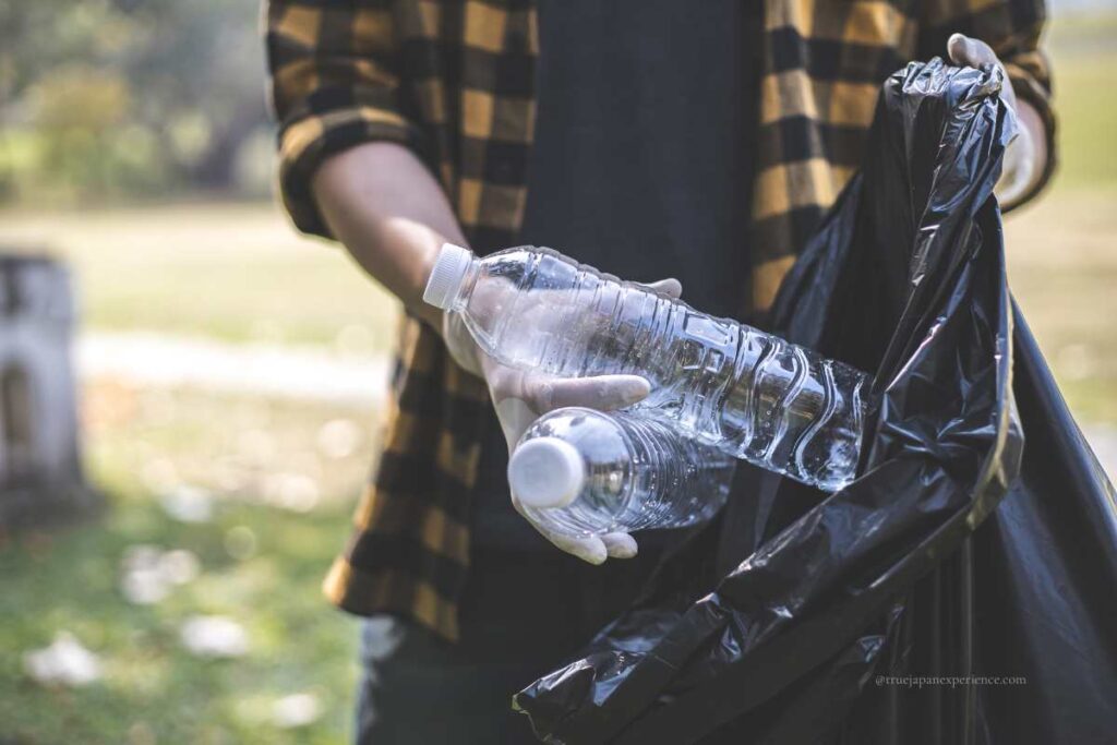 Person wearing picking up plastic bottles and putting them into a garbage bag in a park.
