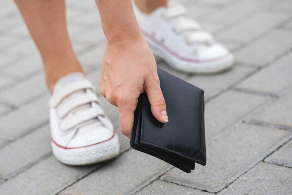 A person picking up a black wallet from the ground while wearing white sneakers
