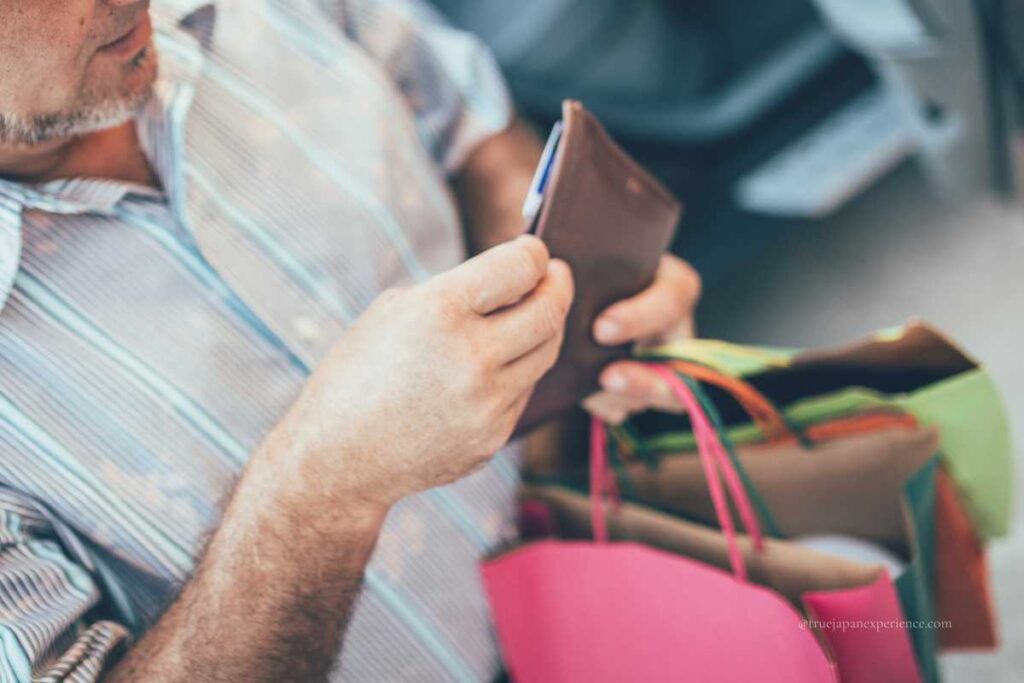 A man holding a brown wallet and several colorful shopping bags