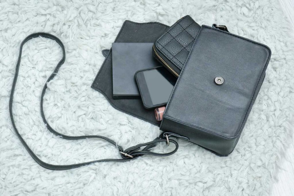 A black handbag lying open on a soft surface with a wallet, smartphone, and other items visible inside