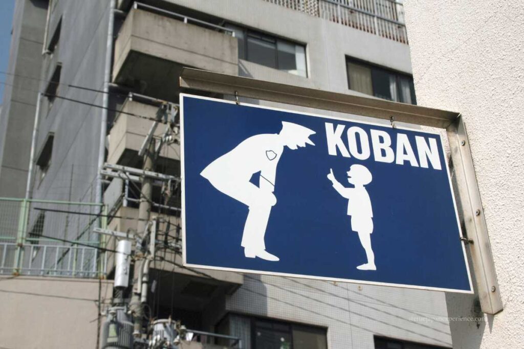 A blue Koban sign showing a police officer talking to a child, mounted on a building wall