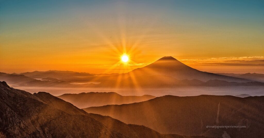 Sunrise over mountain ranges with Mount Fuji in the distance.