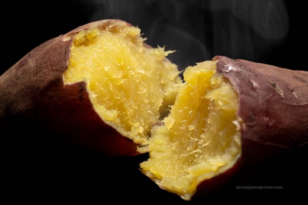 A freshly roasted Japanese sweet potato split open, showing its soft golden inside with steam rising