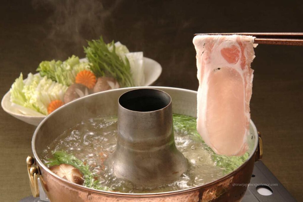 A Japanese shabu-shabu hot pot with a thin slice of pork being dipped into boiling broth with vegetables