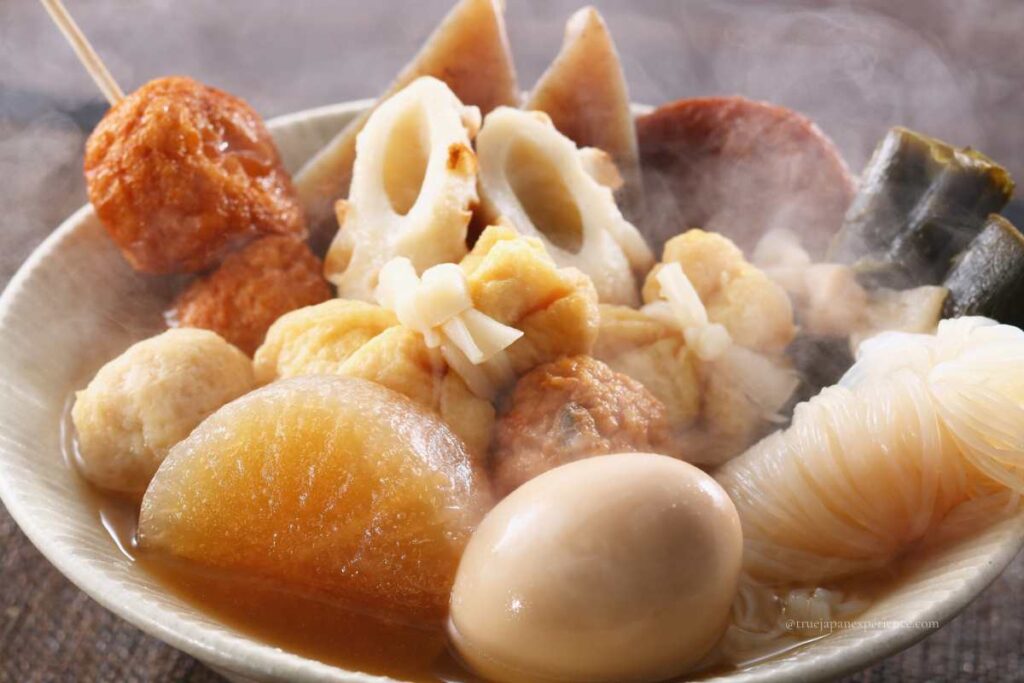 A steaming bowl of Japanese oden with daikon radish, boiled egg, fish cakes, konjac, and kelp in a light soy broth