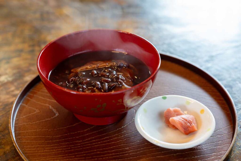 A bowl of Japanese zenzai sweet red bean soup with mochi, served with pickles on the side
