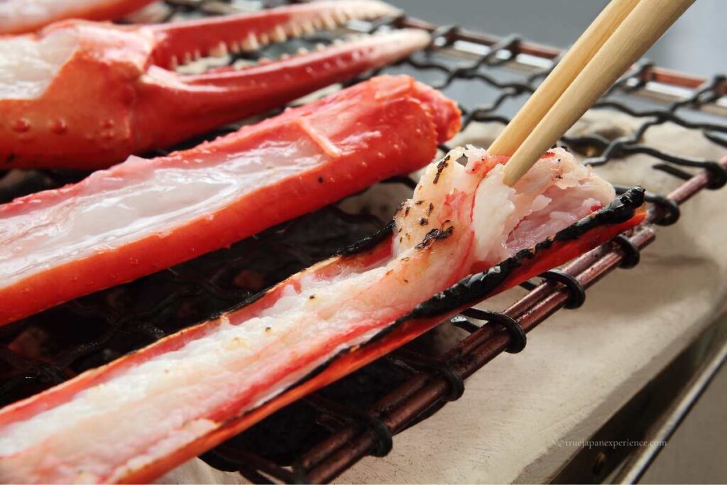 Grilled Japanese crab legs on a charcoal grill, with chopsticks picking up the meat